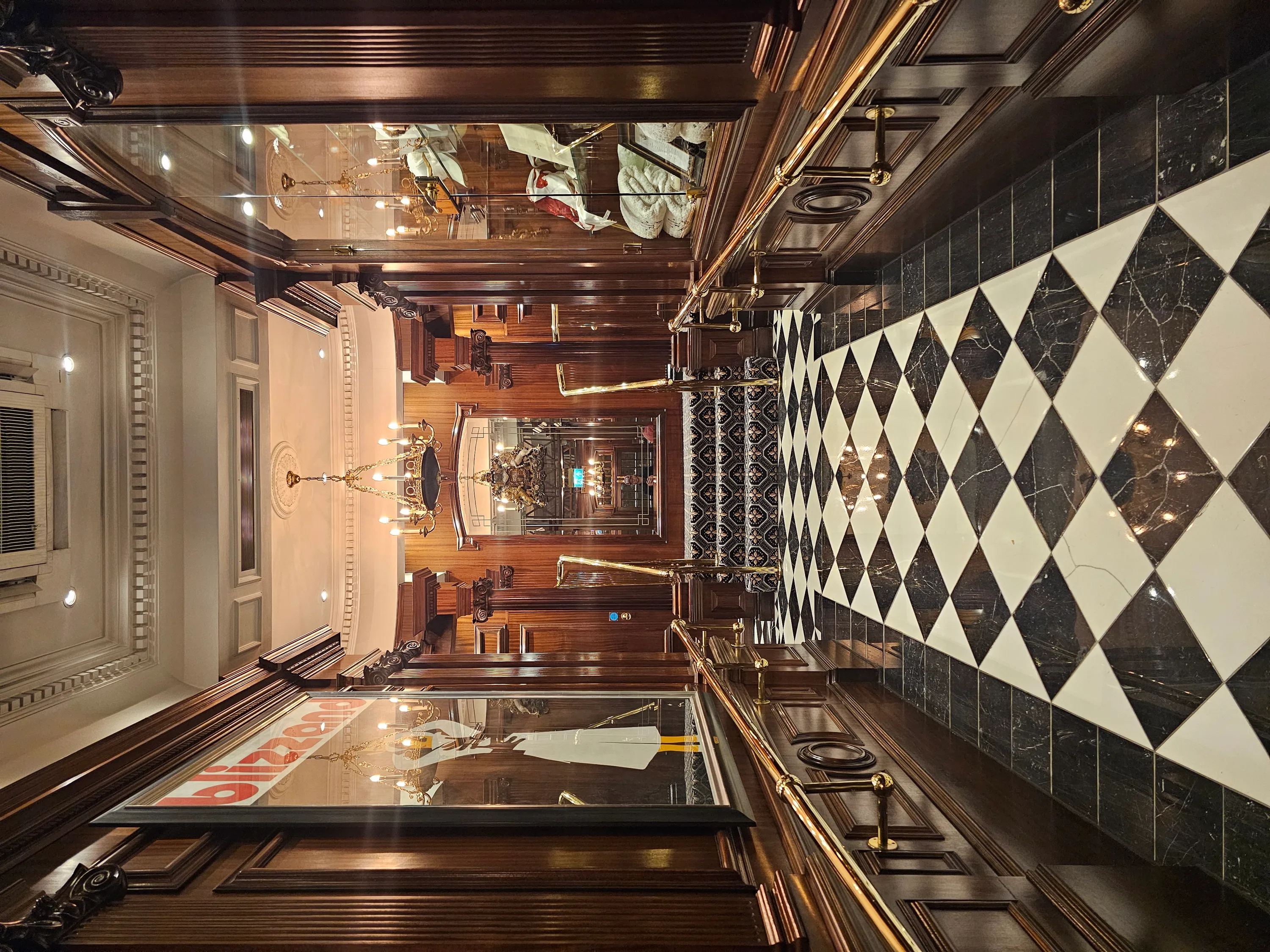 A wood-paneled hotel corridor with a black-and-white tiled floor leading toward reception