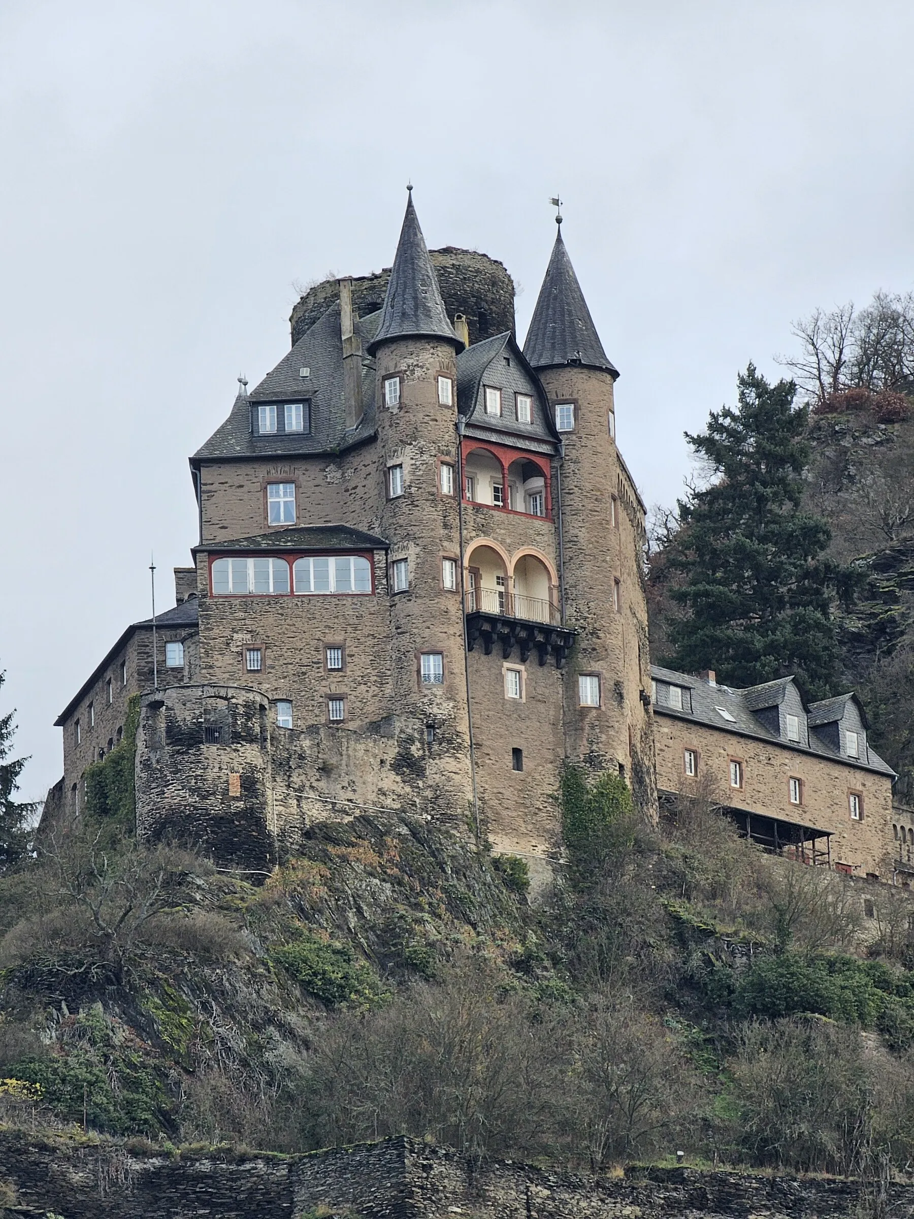 A stone castle rising above a wooded bank along the Rhine