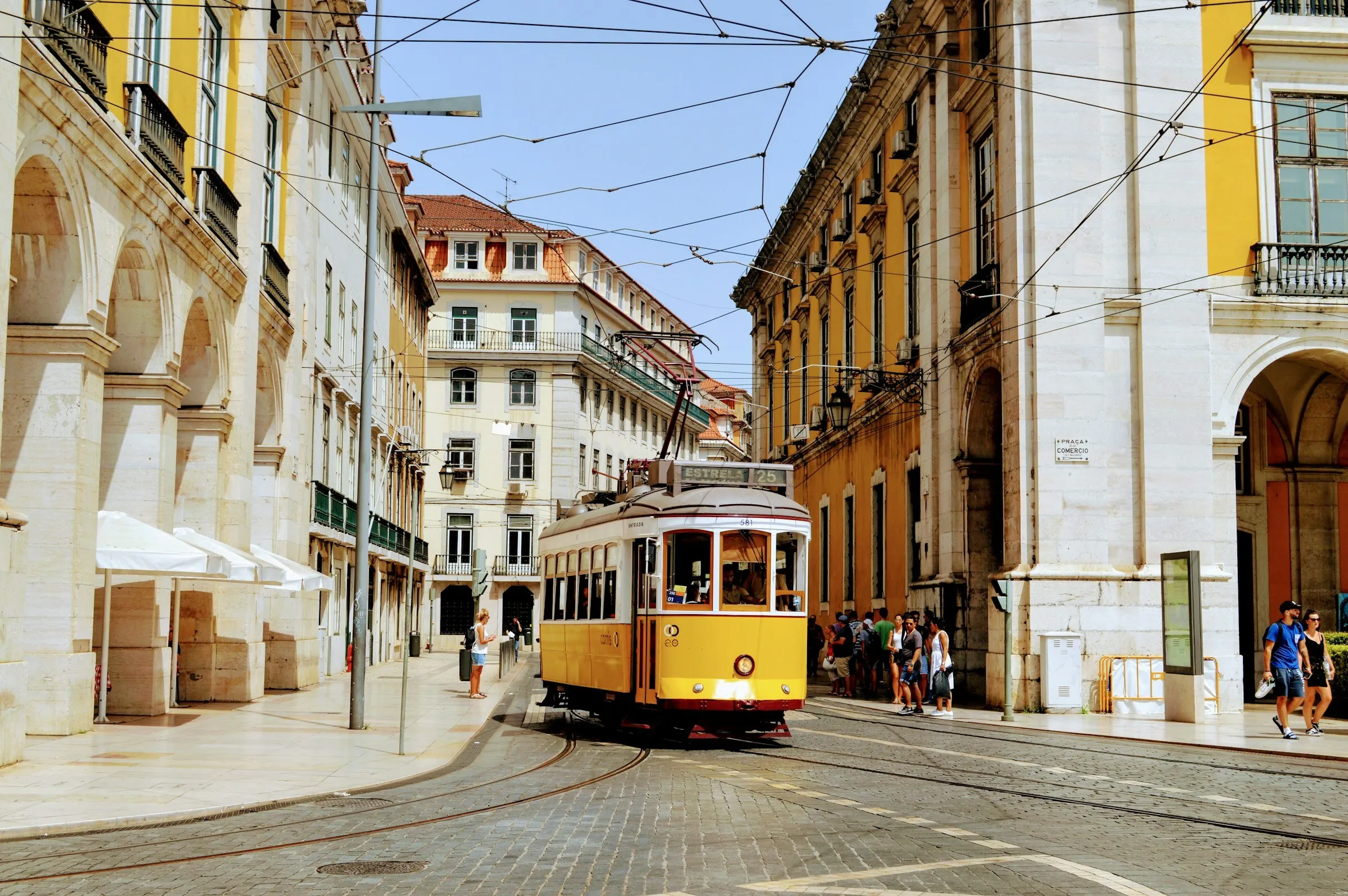 A yellow tram moving through the historic streets of Lisbon